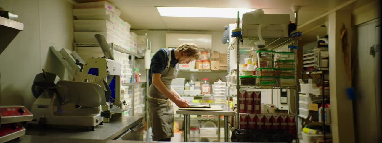 A man looks at a clipboard in the storage area of a kitchen