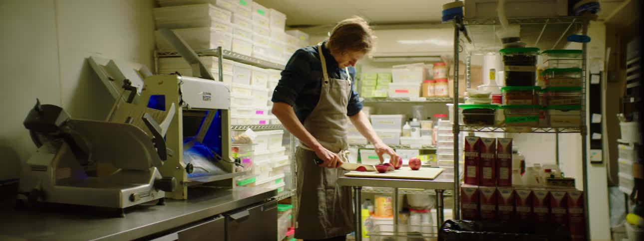 A caucasian male in a kitchen chopping and peeling onions