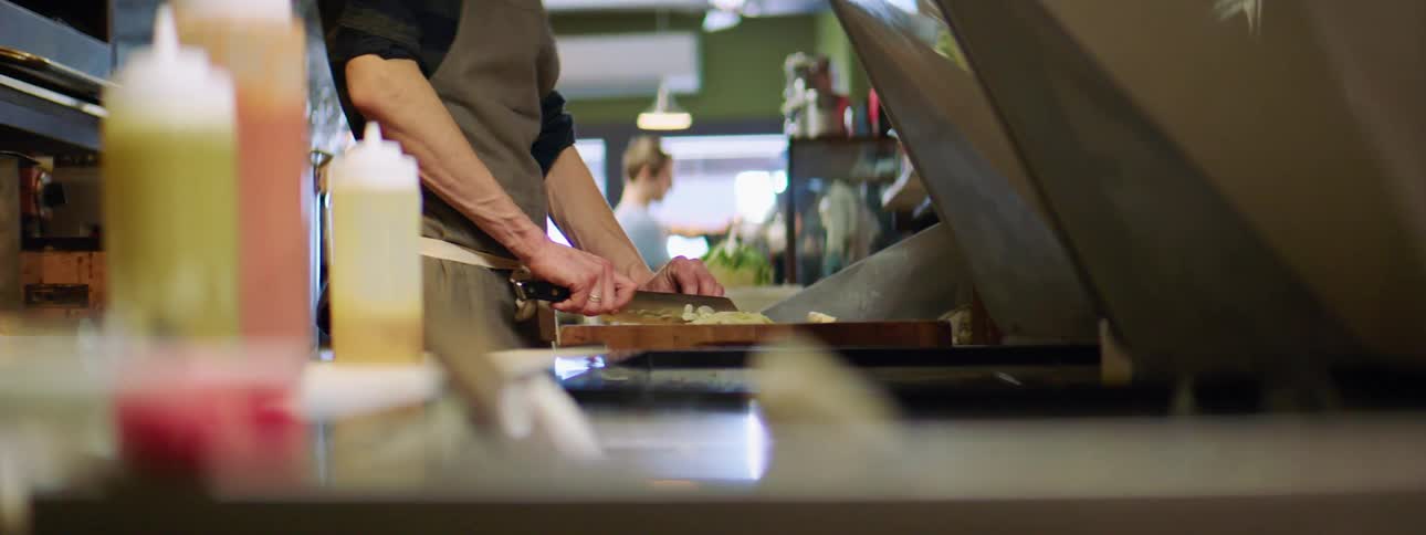 A male caucasian is in a kitchen chopping food