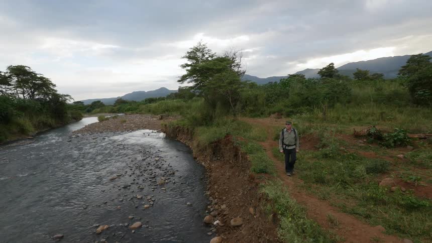 A man walking along a river bank on a cloudy day