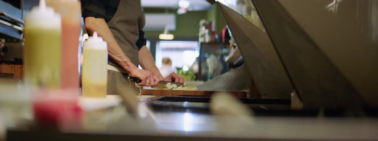 A young man in a gray apron chopping food on a wooden cutting board
