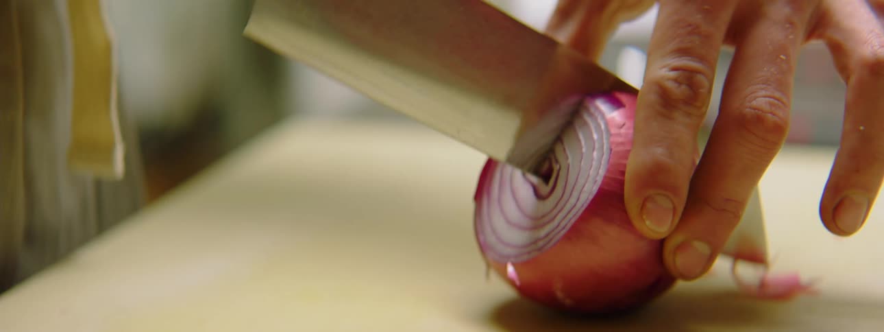 A person uses a knife to cut a red onion