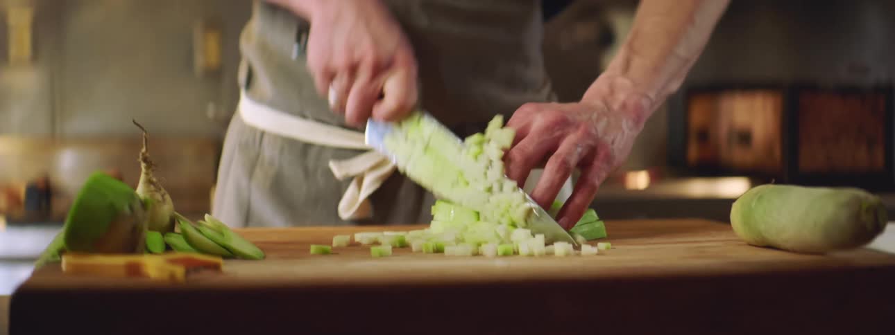 A man dices vegetables in a commercial kitchen
