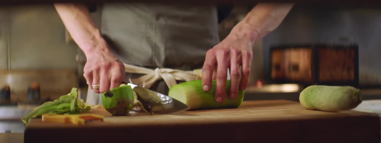 A man with a knife chopping a vegetable in the kitchen