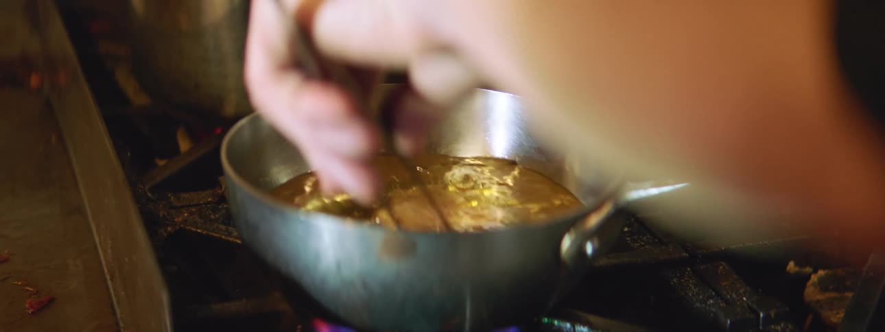 Person dips chicken wing into hot oil in a pan on a stove
