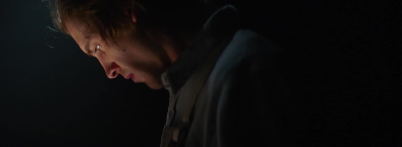 A light shines on a mans face as he looks down working in the dark