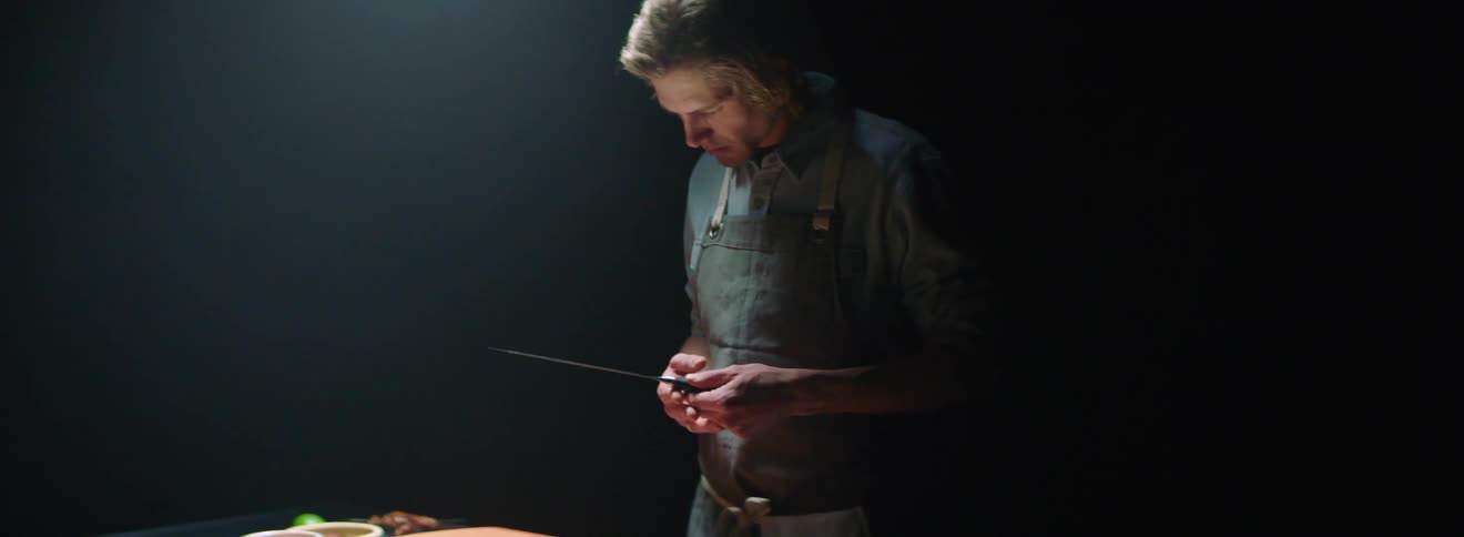 A man in front of a cutting board looking at a knife