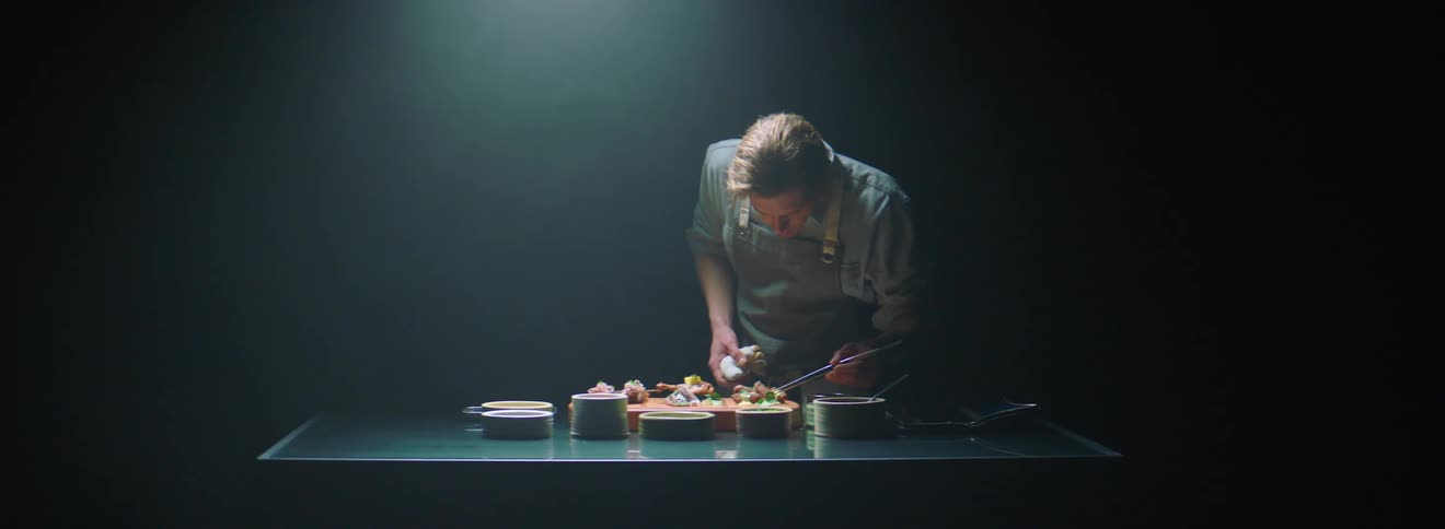 A man is preparing dishes on a table in the dark