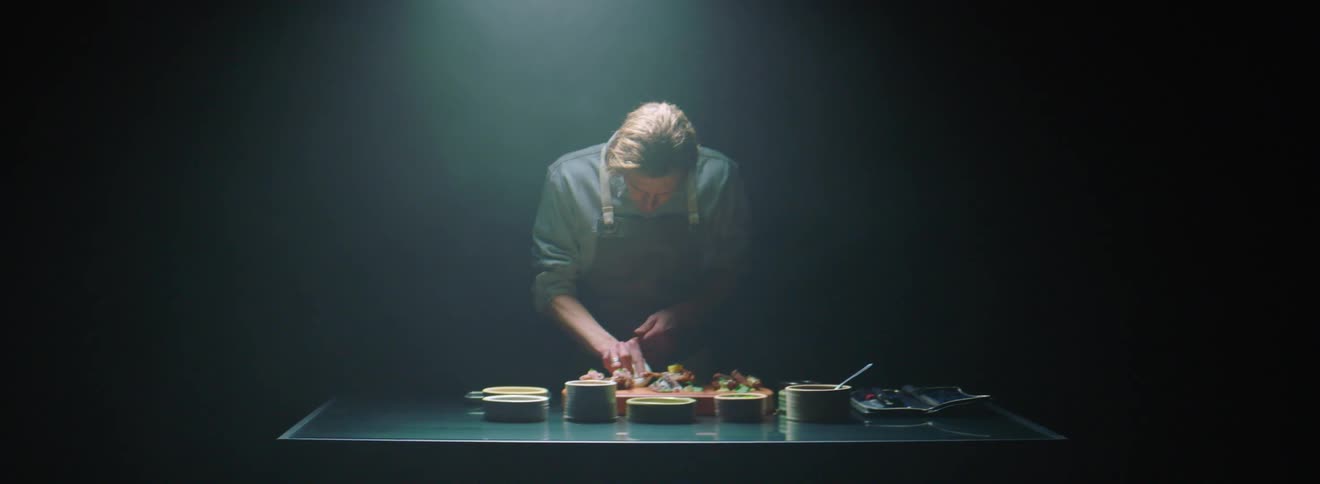 A male chef in a dark room cleaning dishes of plated food