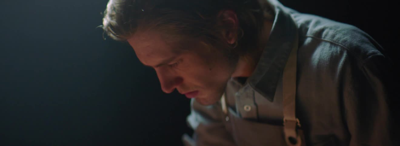 A man wearing an apron looking down as he concentrates and works