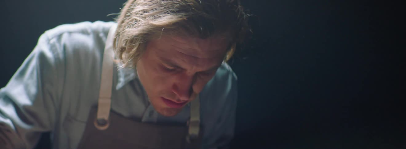A man is bending over concentrating on what he is doing