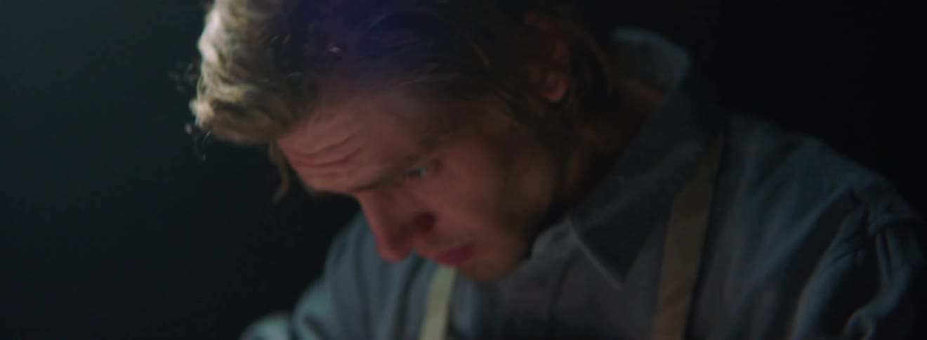 A man wearing an apron works on something below the camera