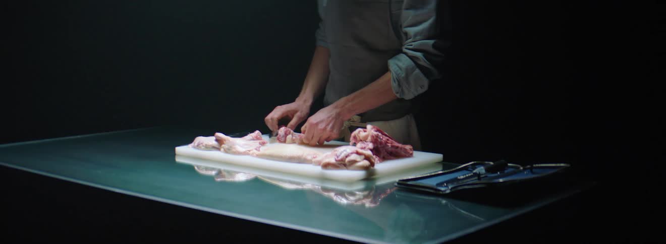 A man using a knife to cut apart raw meat