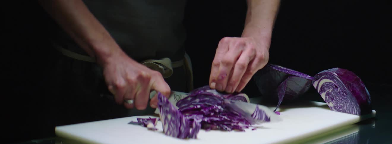 A chef uses a large knife to cut a head of red cabbage