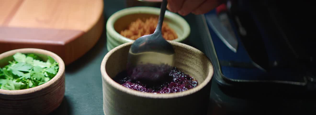 Man stirs the fruit paste with a spoon in the mini bowl in the kitchen during daylight