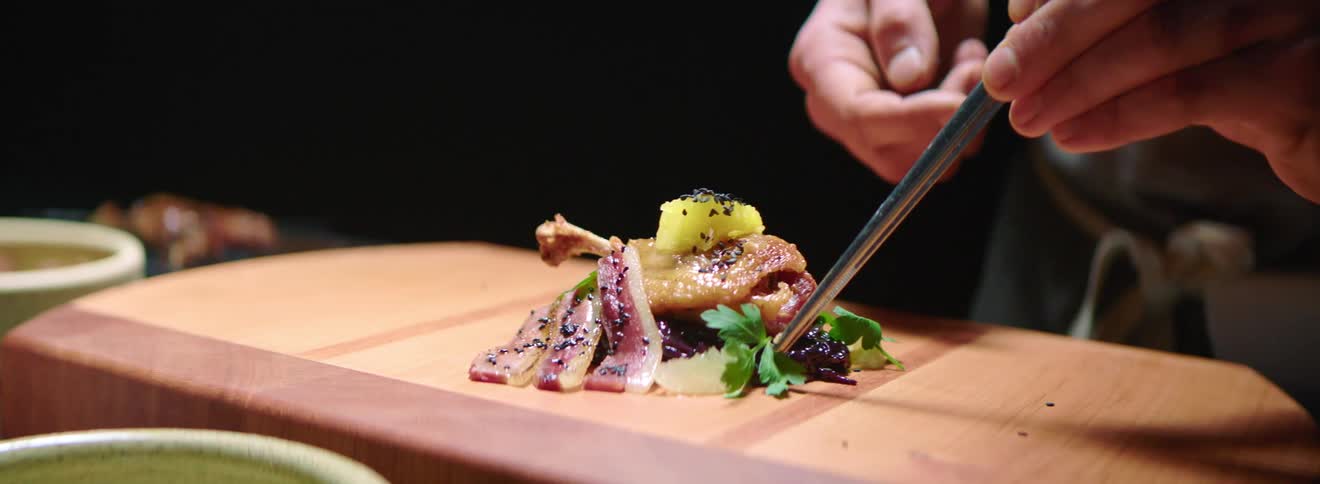 A chef adding finishing touches to a meal plated on a cutting board