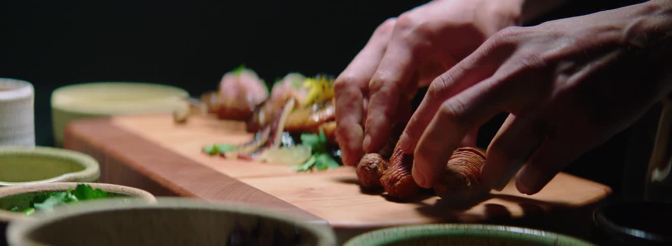 A man in an apron arranges the first serving of a three serving platter on a wooden board