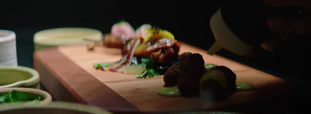 A person squeezes sauce on to a tray with food