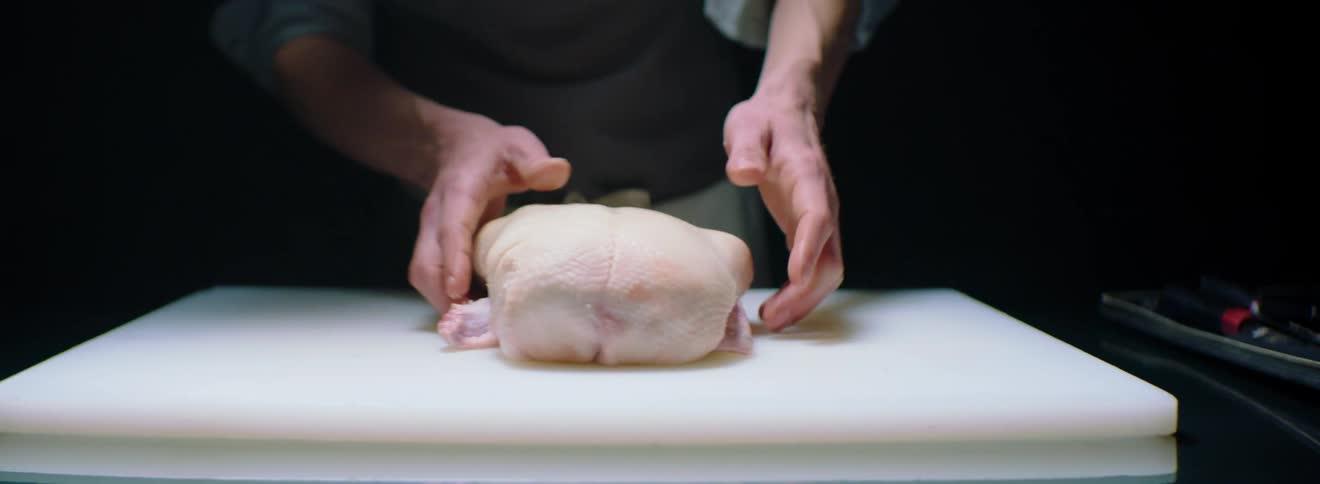 A man is examining a bird on a cutting board