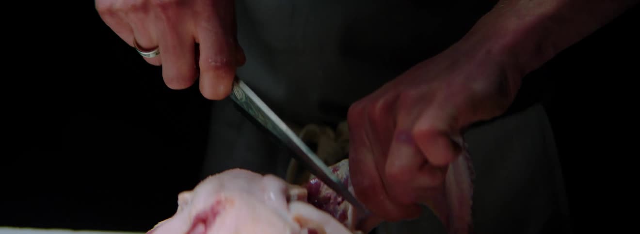 A white man carves a skinless chicken with a knife