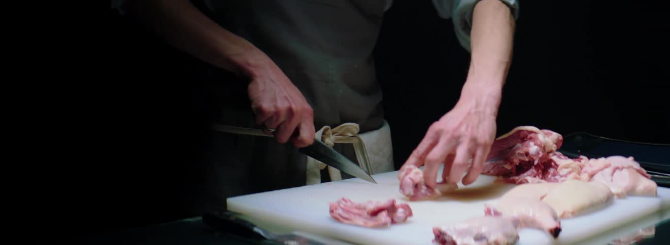 A male caucasian chopping meat on a cutting board