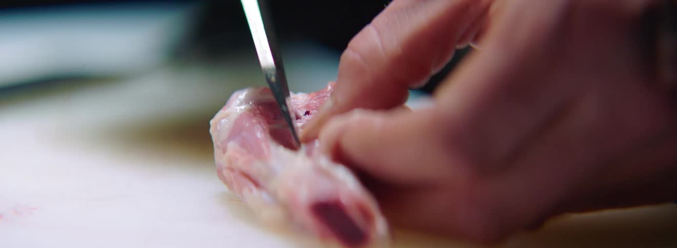 A chef slices meat and skin away from a bone with a sharp knife