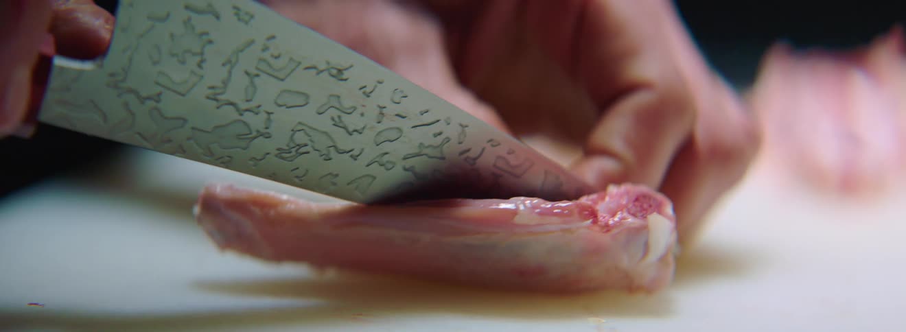 A chef is deboning a piece of meat with a large chefs knife