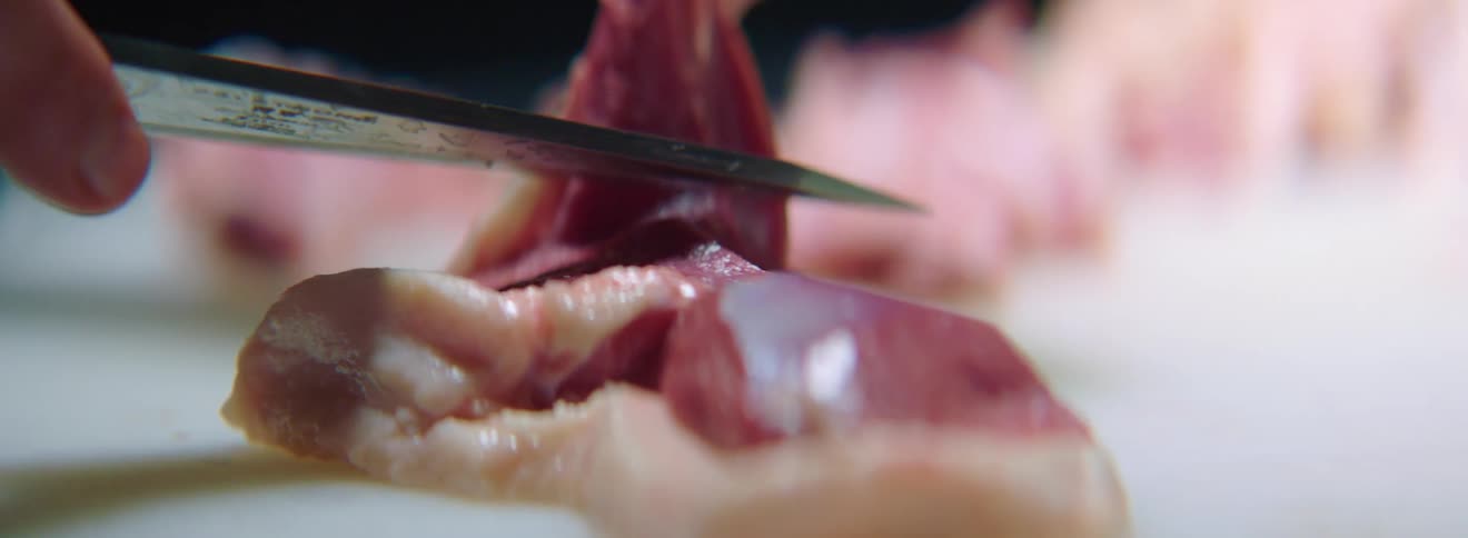 A person is trimming the skin on meat