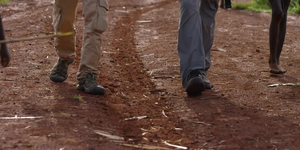 Close up of peoples legs and feet as they walk down a dirt trail