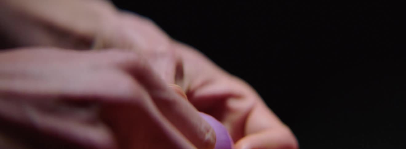 A man peels the skin off half a shallot then puts it down and picks up the other half