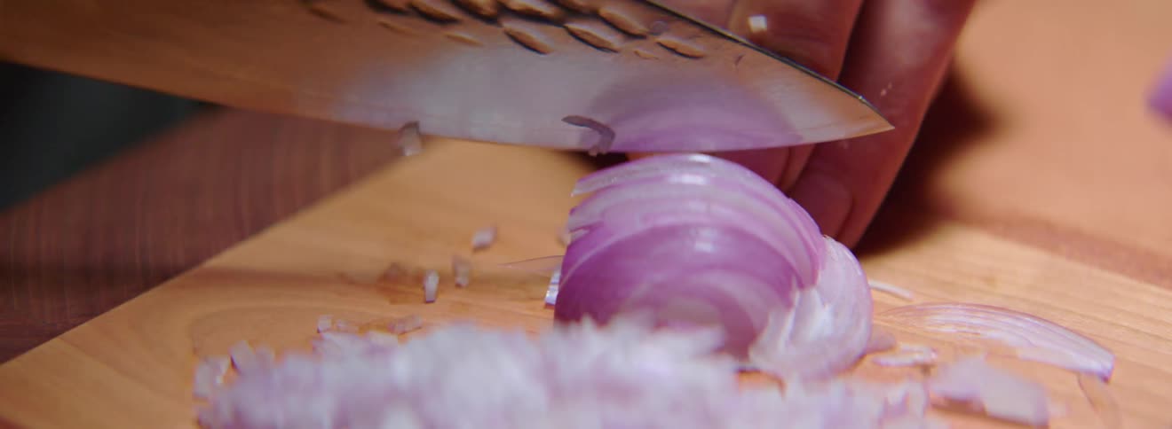 A white man dices a red onion with a sharp cooking knife