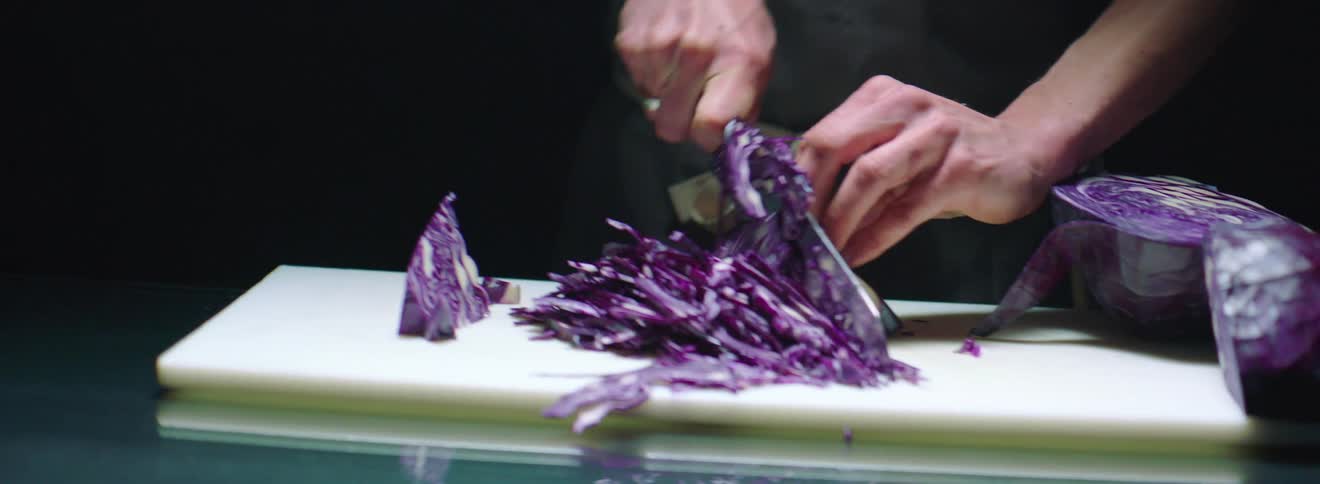 A chef cutting into a large head of red cabbage