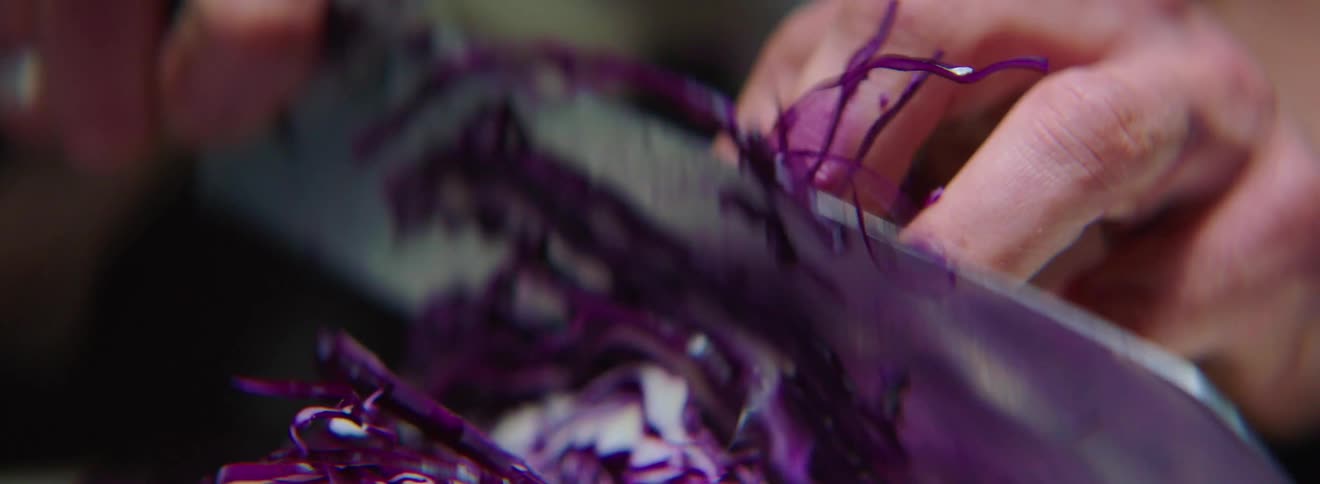 A person chops purple cabbage with a knife
