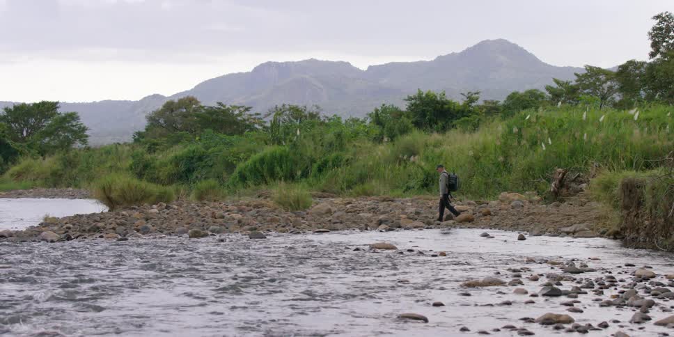 A man is hiking around a stream on a cloudy day