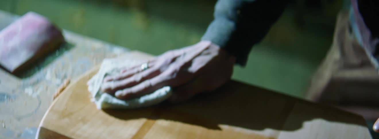 An older white person squirts liquid on a towel and rubs it across a block of wood