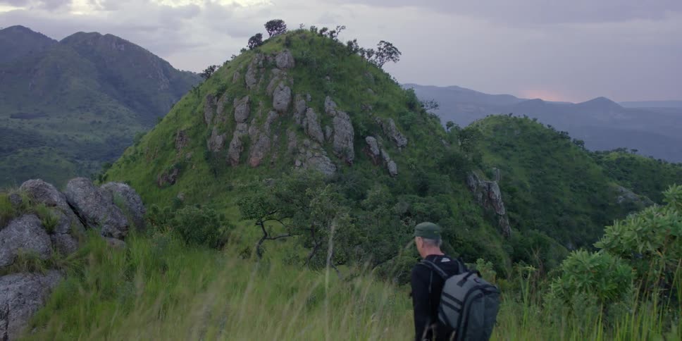 A man is hiking on a mountain covered with grass on a cloudy day
