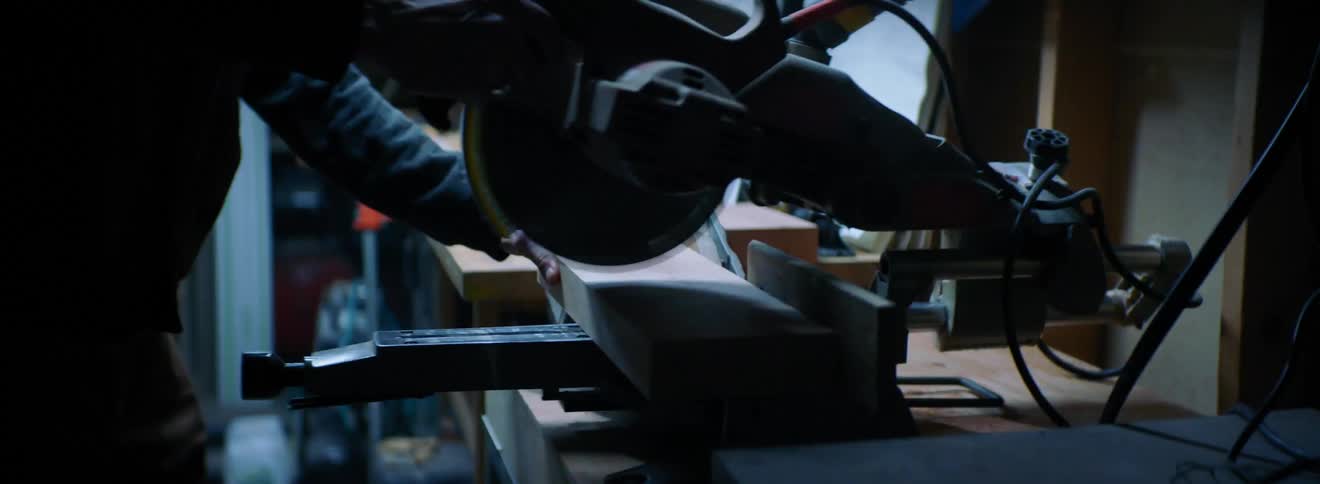 A man uses a table saw to cut a piece of wood in a workshop with flashing lights