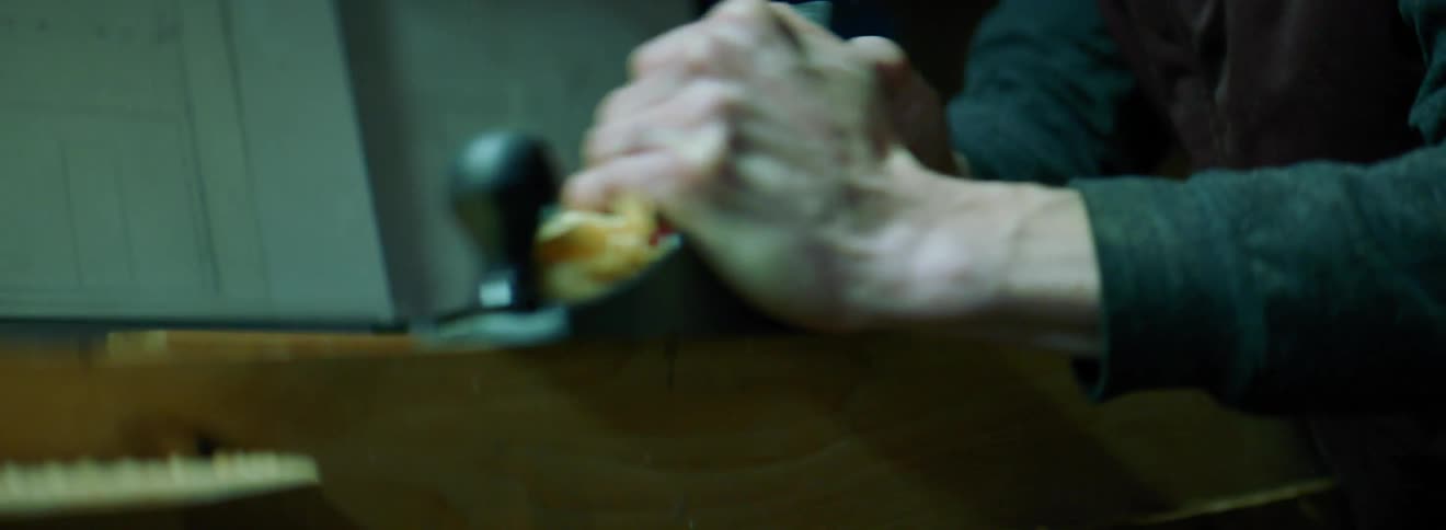 A man uses a hand planer on a board