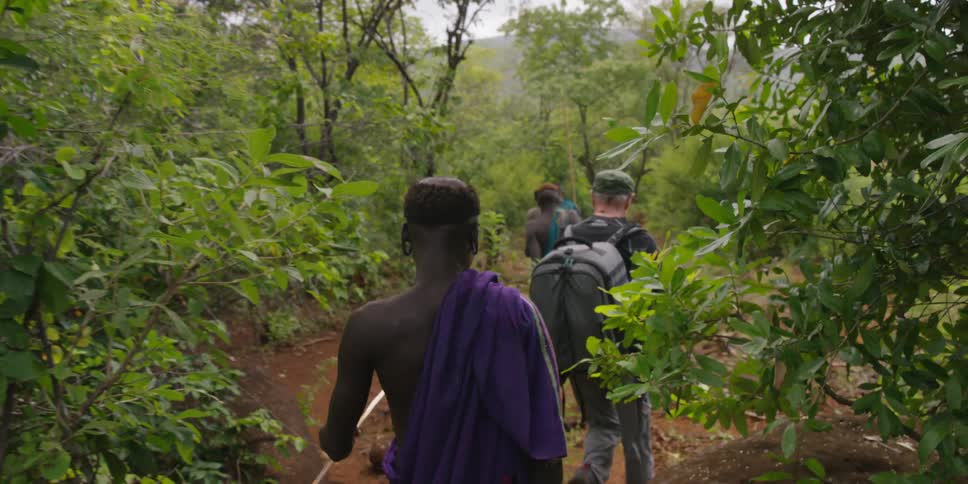 A white man walking along a forest trail with african tribesmen