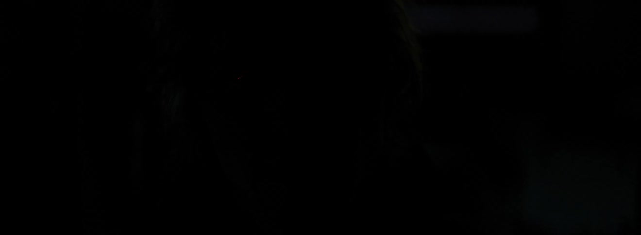 A young white turning his head to stare into the camera while in a dark room with a rapidly blinking light