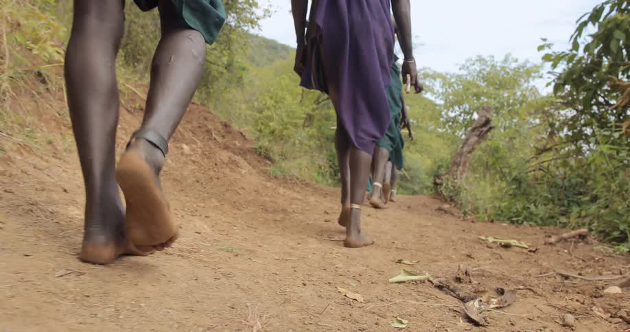A group of people are walking on a trail barefoot