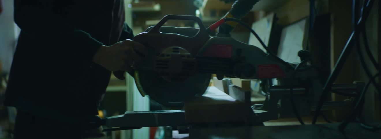 A blonde white man sands a piece of wood on a table