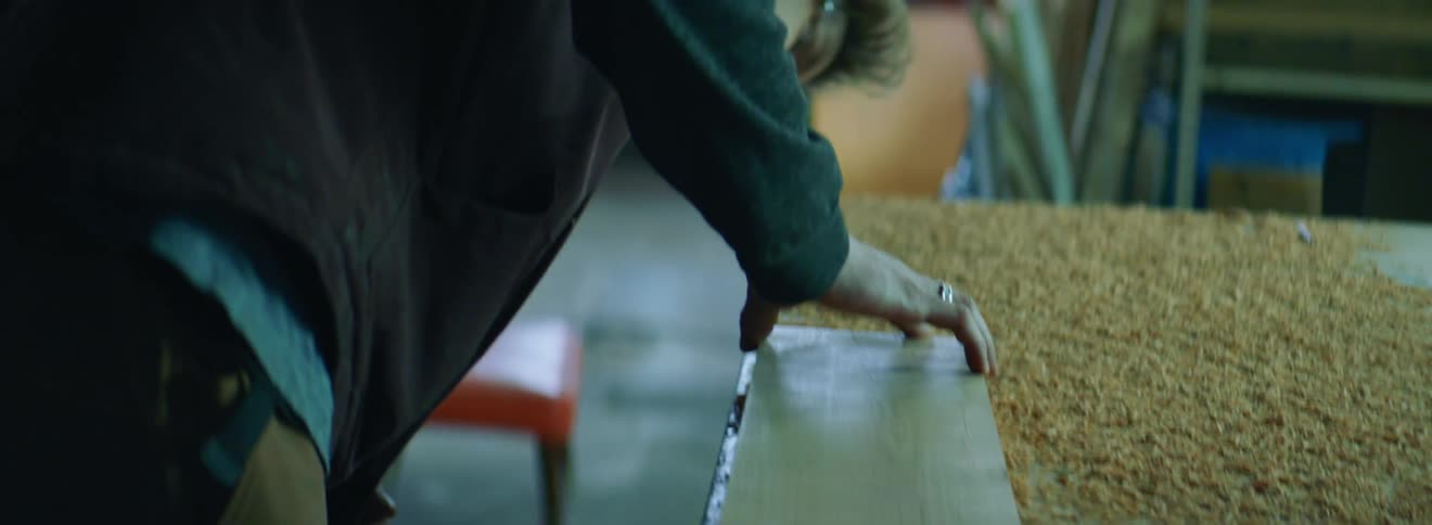 A white woodworker wearing safety goggles in a workshop examining a wooden board