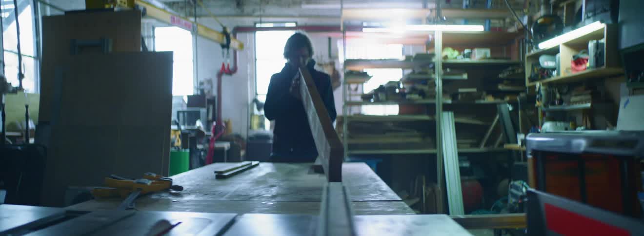 A young man in a workshop inspects lumber for imperfections