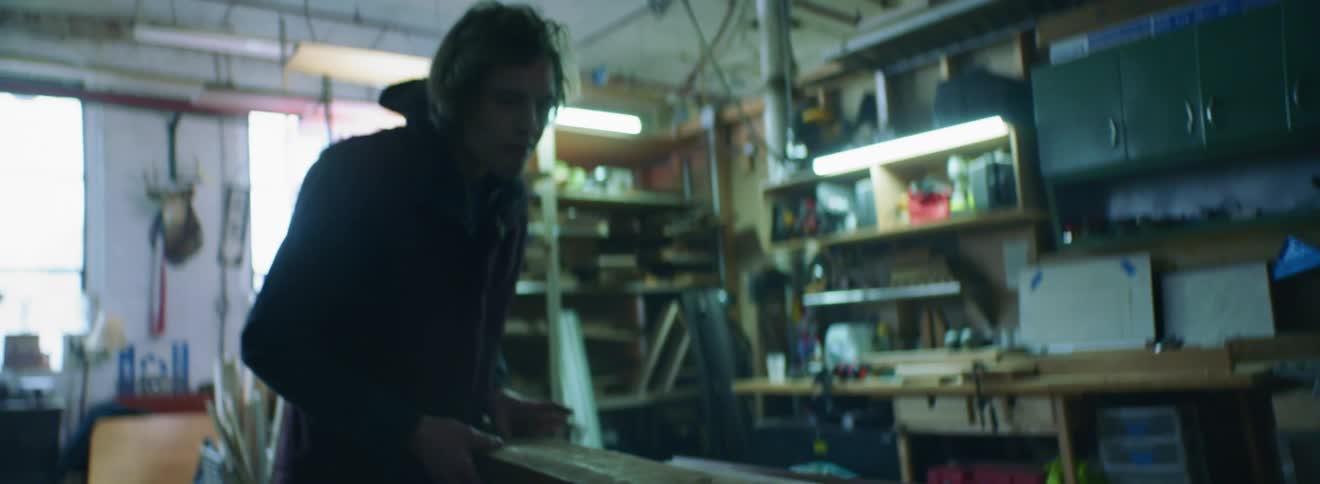 A man in a workshop flipping a piece of lumber on a table