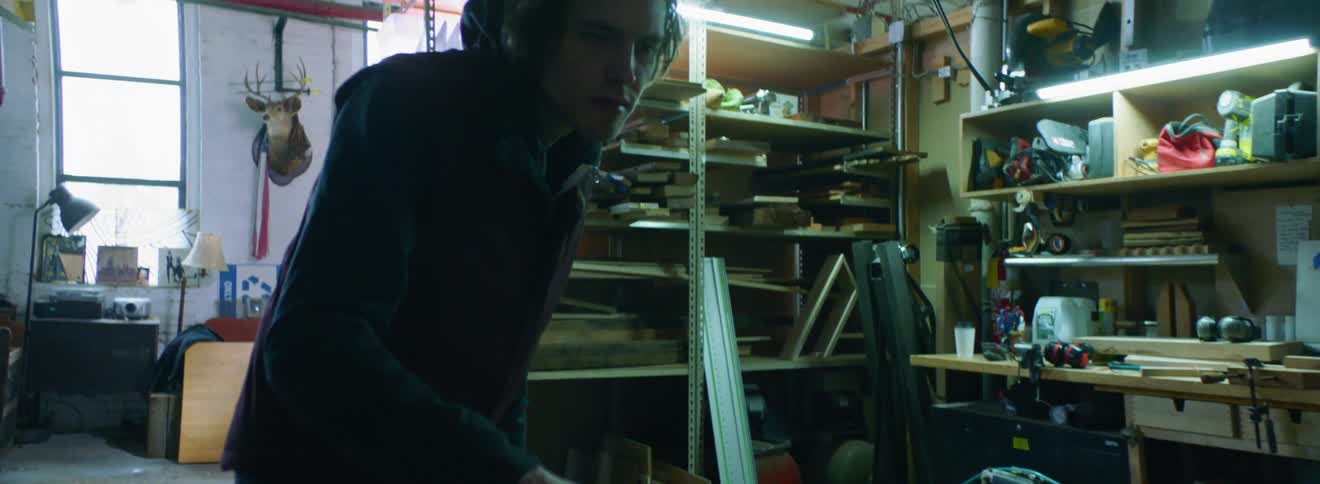 A young white man sizes up a piece of wood in a workshop