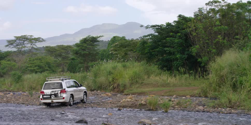 A car drives across a stream on a cloudy day