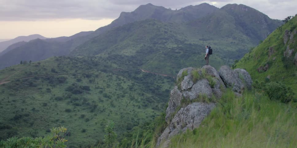 A man with a black backpack stands on a rock near a mountain