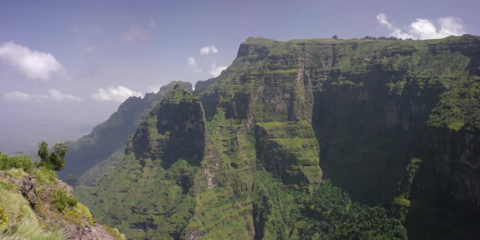 A man walks to the edge of a cliff on a clear day