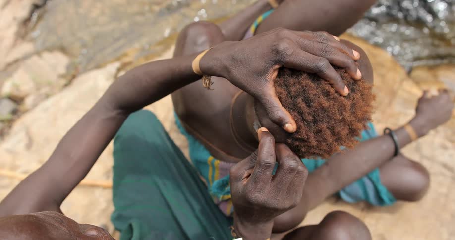 An african tribesman man using a razor blade to shave the head of another man